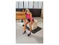 Lachende vrouw in roze top en zwarte shorts, zittend op een springbox, met een oranje waterfles.