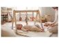 Baby ligt onder houten speelboog met hangend speelgoed, persoon ernaast.