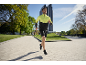 Homme en veste de course jaune et noire et short noir faisant du jogging en extérieur.