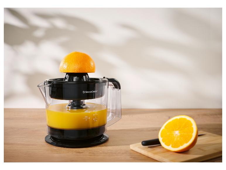 Presse-agrumes Silvercrest avec oranges et jus sur un comptoir en bois.