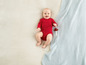 Un bébé en pyjama rouge est allongé sur une couverture avec un jouet.