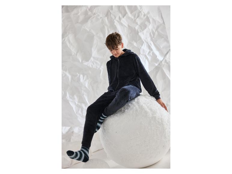 Jongen in zwarte pluche pyjama, gestreepte sokken, zittend op een grote sneeuwbal.