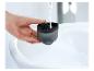 Main remplissant un récipient noir avec de l'eau du robinet au-dessus d'un évier blanc.