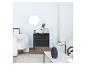 Commode noire à tiroirs, fauteuil blanc et miroir rond dans un salon.