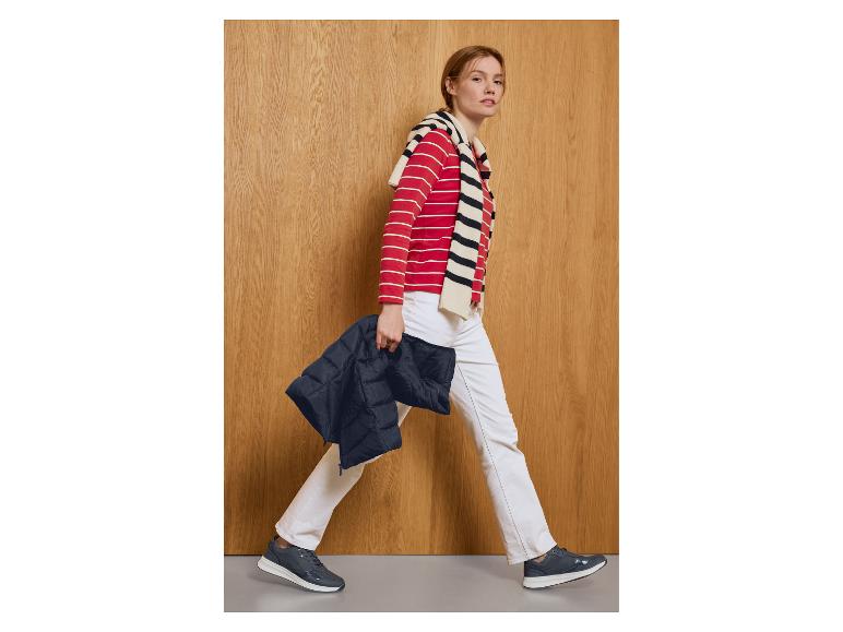 Vrouw in rood-wit gestreepte top, witte broek en donkerblauwe sneakers, met een donkerblauwe jas.