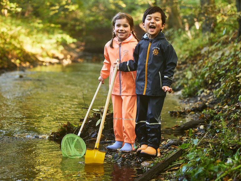 Twee kinderen in regenkleding spelen met een schepnet en een schep in een beek.