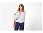 Femme souriante en pull blanc, pantalon bleu marine et veste beige sur l'épaule