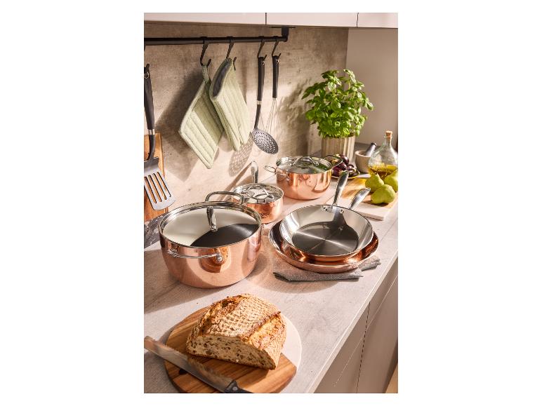 Ensemble de casseroles en cuivre avec casseroles et poêles sur un comptoir de cuisine avec des ingrédients frais.