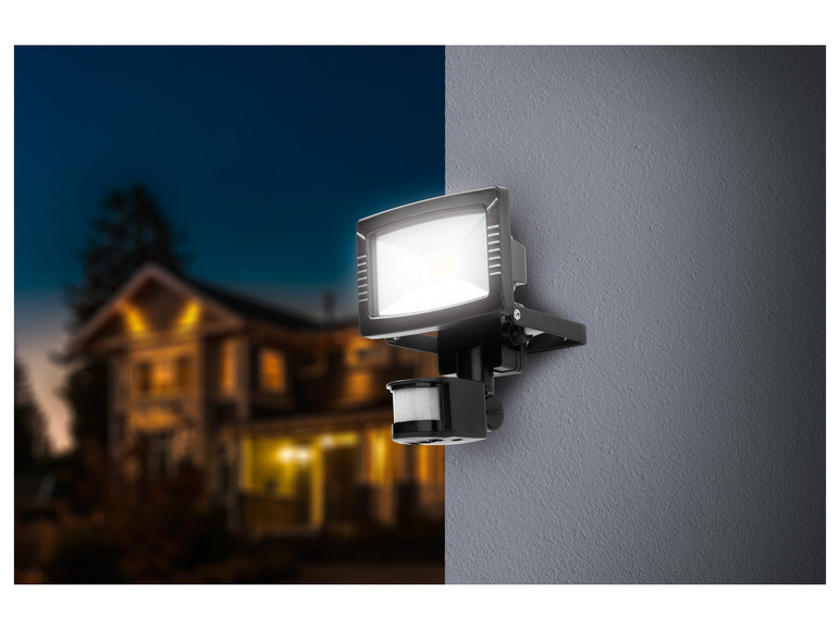 Un lampadaire extérieur noir avec détecteur de mouvement, fixé à un mur gris.