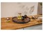 Plateau en bois avec théière en verre, tasses noires, biscuits et sucre sur un comptoir en bois.