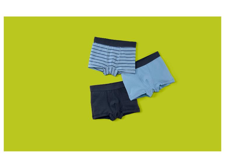 Drie jongensboxershorts in blauw en marineblauw, één gestreept, op een limoengroene achtergrond.