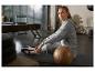 Femme en survêtement gris assise sur un tapis d'exercice avec un ballon en cuir.