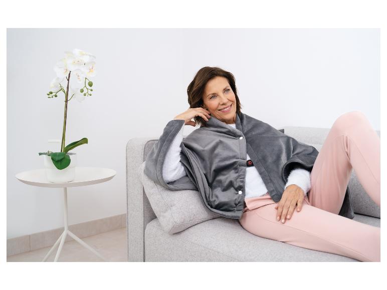 Une femme assise sur un canapé avec une couverture chauffante grise.