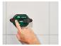 Une main appuie sur un bouton d'un mètre laser Parkside sur un mur de carreaux blancs.