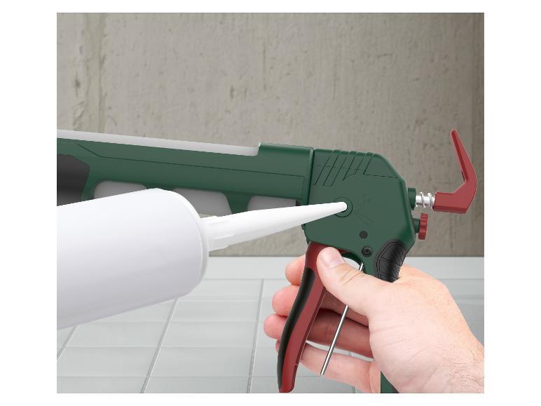 Een hand houdt een groen en rood kitpistool vast met een witte kitkoker erin.