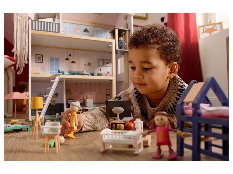 Een kind speelt met een poppenhuis en kleine figuren op een houten vloer.