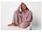 Lachende vrouw in roze pyjama, zittend op een stoel.