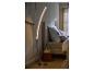 Lampadaire LED incurvé éclairant une chambre moderne avec lit et table de chevet.