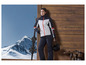 Een vrouw in een skipak met een skibril en ski's voor een houten muur.
