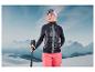 Een vrouw in ski-kleding met een zwarte jas, roze broek en ski-stokken in een besneeuwde bergachtige omgeving.