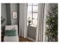 Salon avec rideaux gris, fauteuil blanc avec coussins verts et grande plante.
