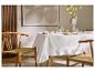 Eettafel met wit tafelkleed, servies, vaas met bloemen en houten stoelen.
