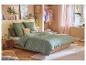 Slaapkamer met groen dekbed en kussens met bloemen, houten bed en lichte decoratie.