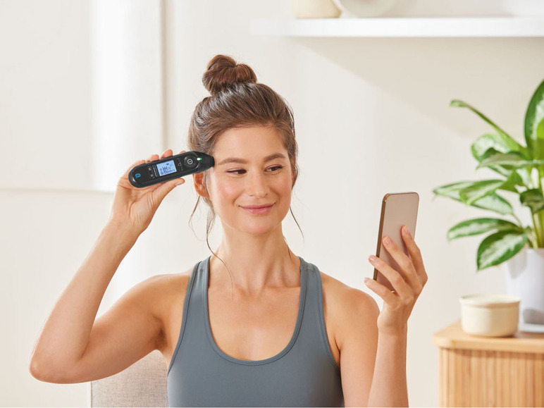 Een vrouw gebruikt een thermometer en haar telefoon.