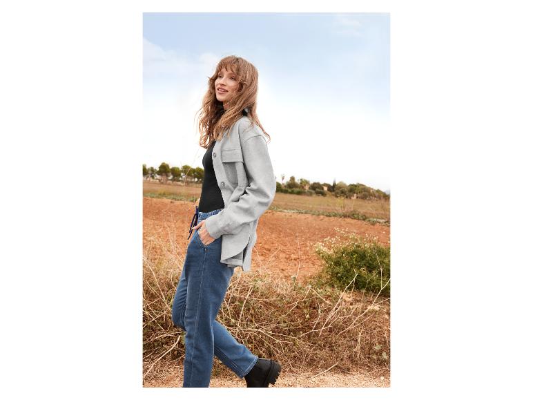Une femme porte une chemise grise, un jean bleu et des bottes noires.