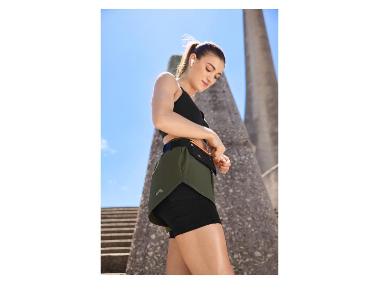 Femme en brassière de sport noire et short de course vert olive avec une pochette pour téléphone.