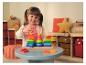 Fillette souriante jouant avec des jouets d'empilage en bois colorés sur une table grise dans une salle de jeux.