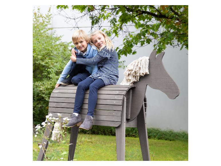Twee kinderen spelen op een houten hobbelpaard in een tuin.
