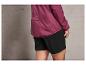 Een vrouw draagt een roze windjack met het woord 'ACTION' erop en zwarte shorts.
