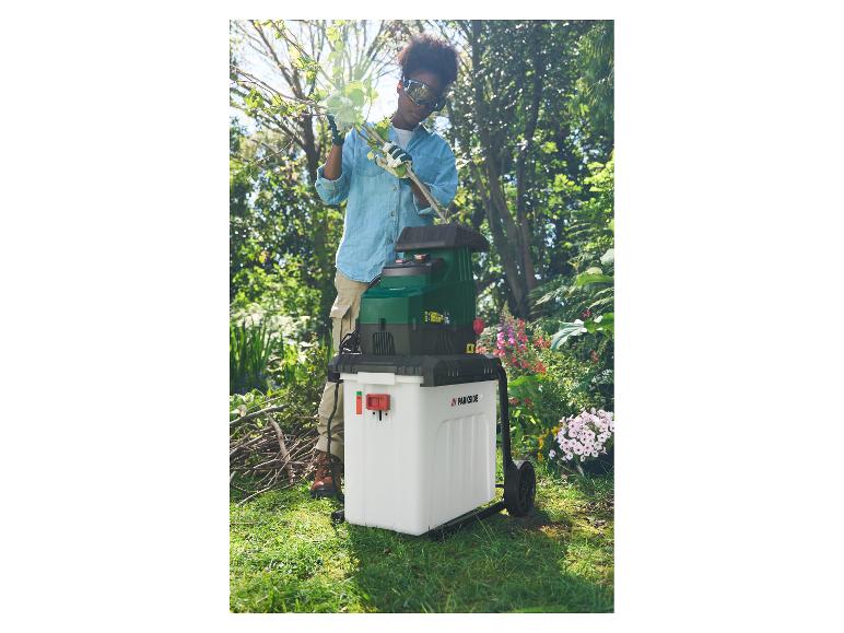 Vrouw in de tuin gebruikt een Parkside takkenversnipperaar om takken te versnipperen.