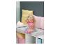 BABY born pop met blond haar, roze top en regenboogrok, zittend op een bankje.