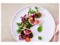 Salade met vijgen, cherrytomaten en groene bladgroenten op een wit bord.
