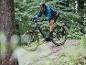 Een man rijdt op een grijze elektrische mountainbike met Maxxis-banden door een bos.