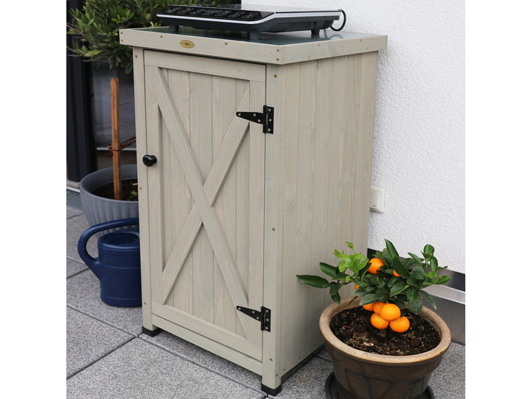 Een houten opbergkast met een paneeldeur, een grill en planten op een patio.