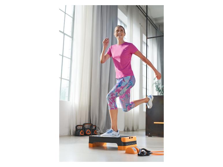 Femme en t-shirt de sport rose et step noir-orange s'entraînant
