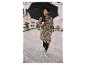 Vrouw in een luipaardprint jas en bijpassende regenlaarzen, onder een zwarte paraplu.