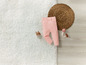 Un pantalon rose pour bébé sur un tapis blanc, avec un cercle tissé et des jouets en forme de champignons.