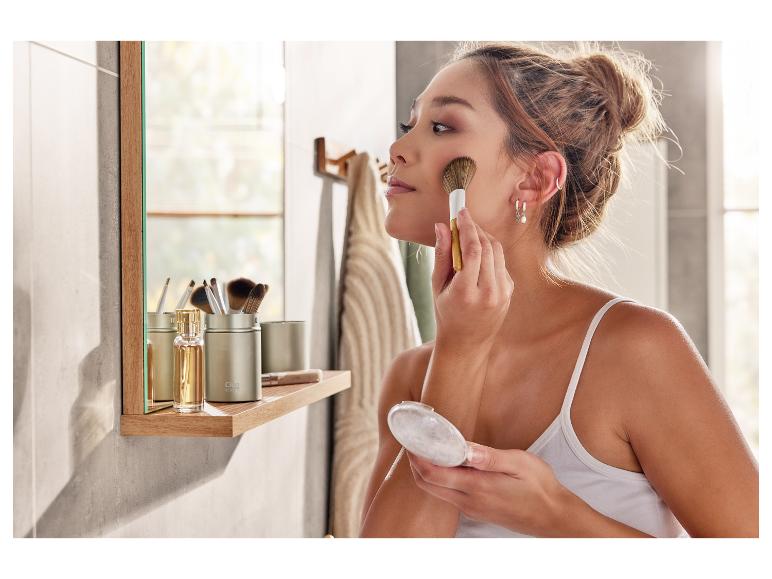 Une femme se maquille avec un pinceau et une poudre compacte dans une salle de bain.