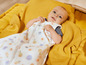 Een baby in een slaapzak met fruitprint, liggend op een gele deken.