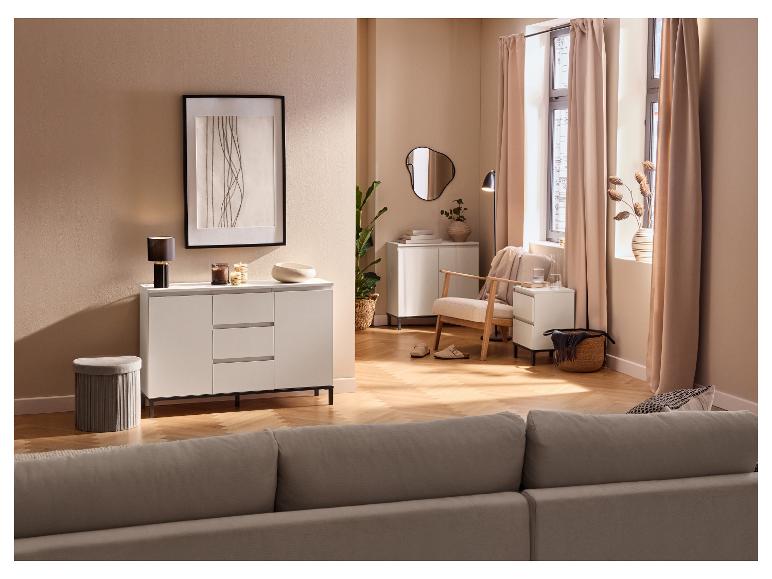 Beige woonkamer met ladekast, fauteuil, nachtkastje en bank.