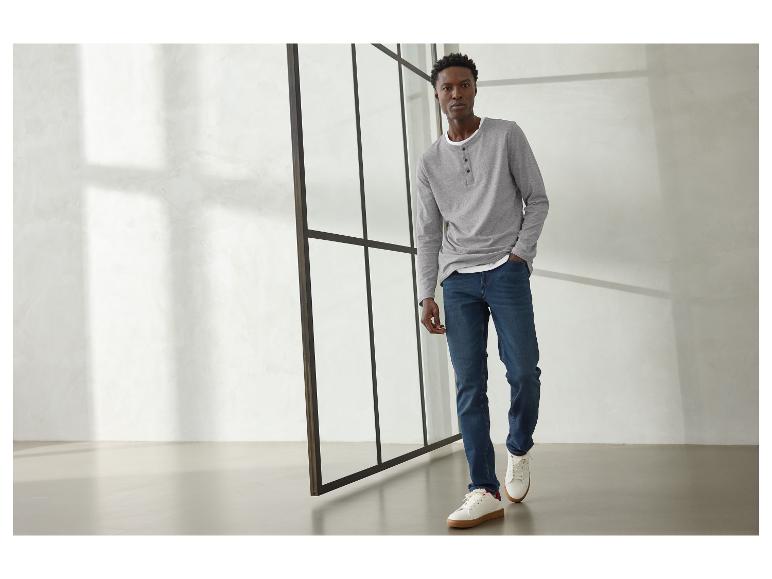 Homme en t-shirt gris à manches longues, jean bleu et baskets blanches.