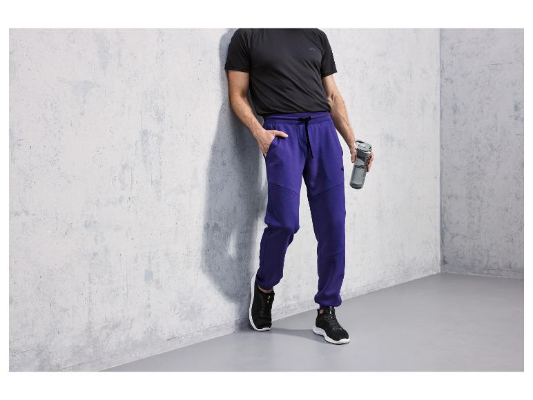 Man in zwarte T-shirt en blauwe joggingbroek met waterfles.