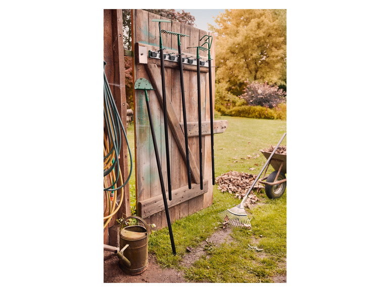 Tuingereedschap, zoals een hark, spade en schoffel, hangt aan een houten schuurdeur.