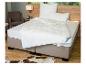 Lit avec matelas blanc, couettes et oreillers matelassés BeCo, avec fauteuil et table de chevet.