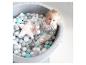 Un bébé joue dans une piscine à balles avec des balles blanches, grises et turquoise.
