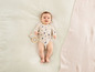 Een baby in een onesie met dierenprint ligt op een deken met een houten rammelaar.